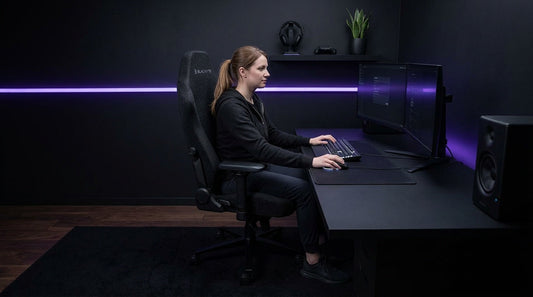 Gamer at an all-black stealth battlestation in an ergonomic matte black gaming chair — long session lumbar support setup