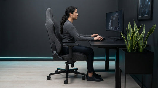 Side-view of a gamer in an ergonomic charcoal-grey fabric gaming chair, feet flat and upright — fabric chair posture support